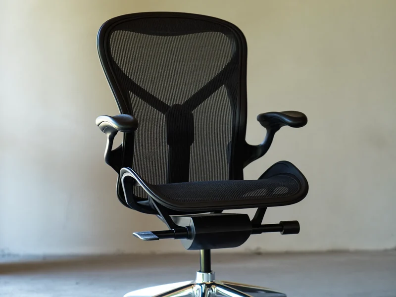 Fauteuil de bureau ergonomique en maille avec soutien lombaire, devant un mur de plâtre clair.