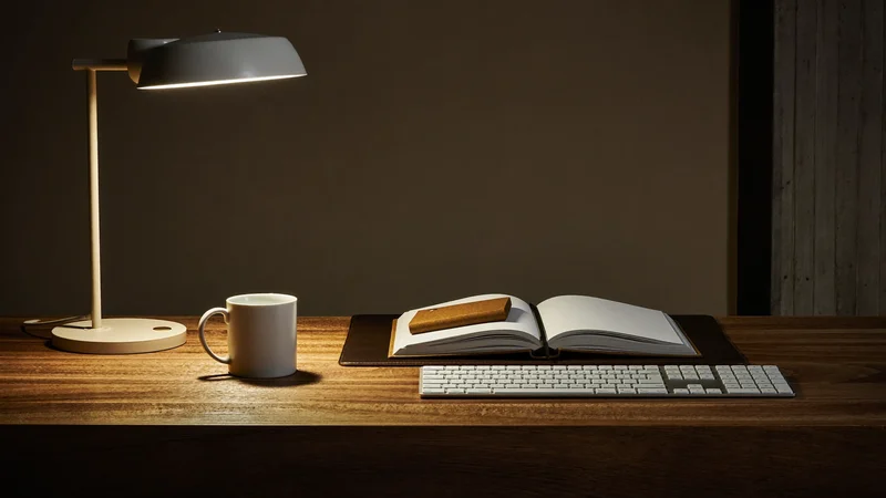 Poste de travail du soir avec lampe, carnet vierge, tasse en céramique et clavier.
